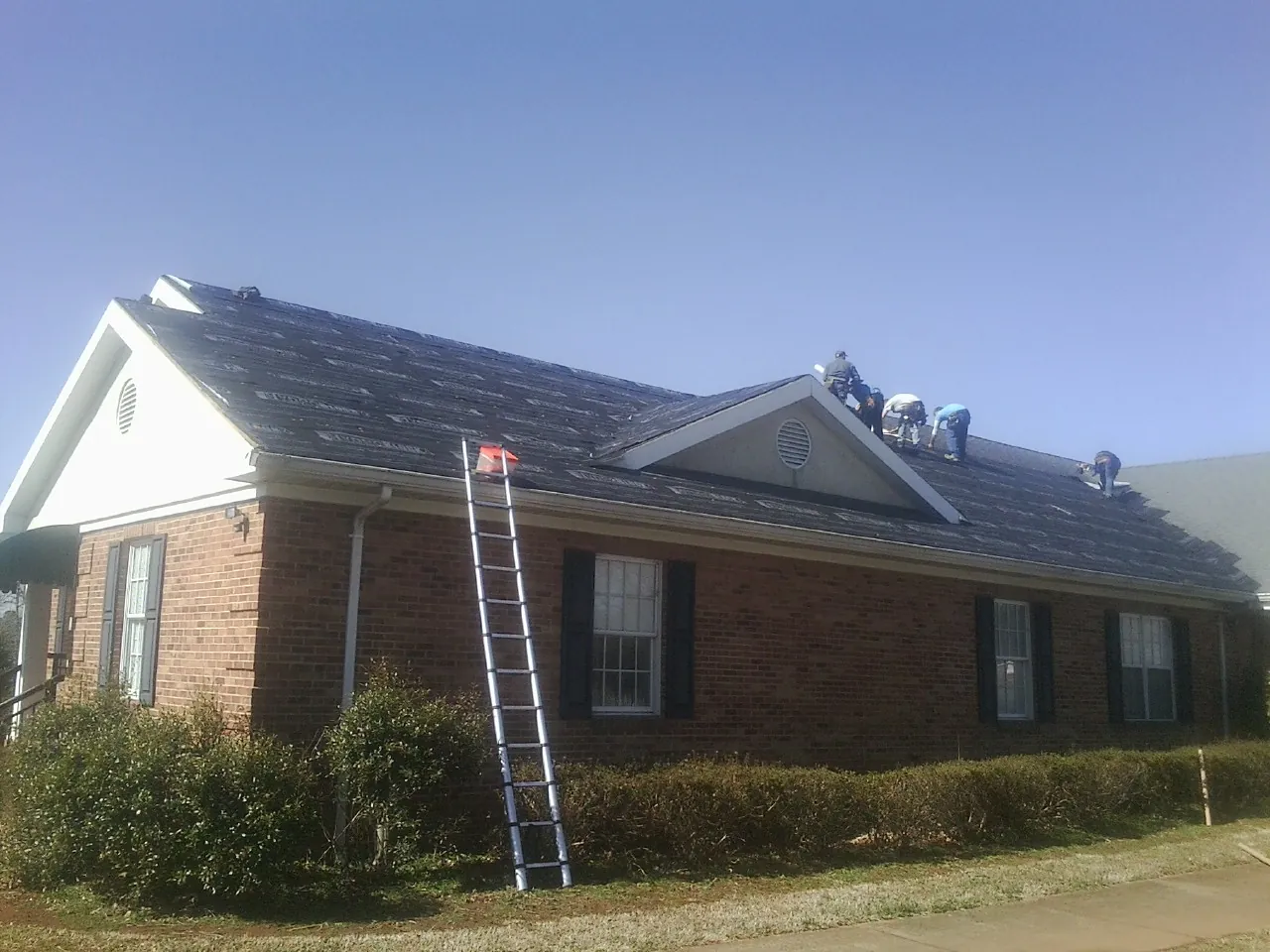 Crew tearing shingles off a brick ranch roof with a ladder set — Metal Roof Repair work by our crew in Scotch Plains
