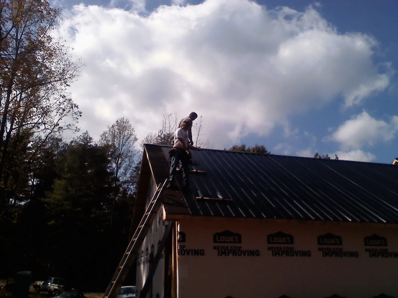 Roofer fastening dark metal panels high against a cloudy sky, from a Roof Inspection job in Scotch Plains