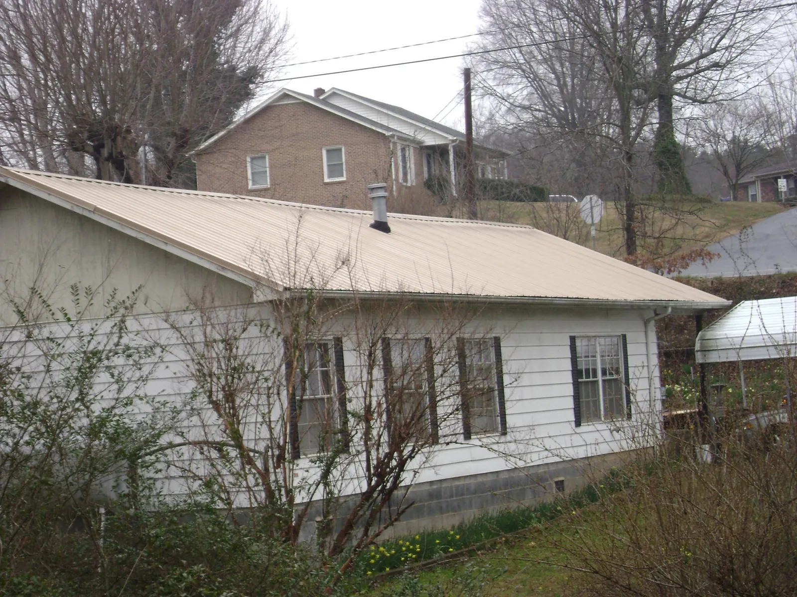 Tan metal roof on a white sided house set into a hillside — Commercial Roofing by Roofing Brothers in Scotch Plains